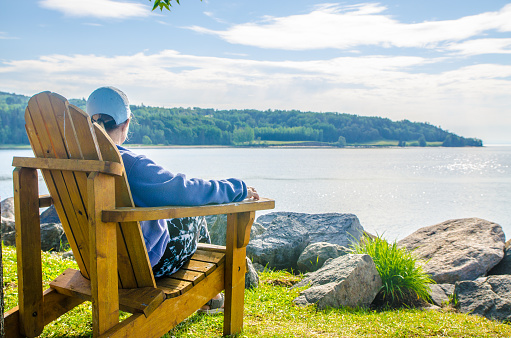 Woman in adirondack chair looking at St. Lawrence river in La malbaie during summer day