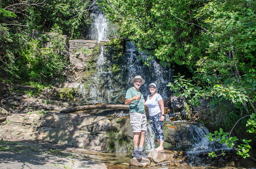 Mature woman and man posing with small waterfall at Cap à l'aigle in La Malbaie during summer day