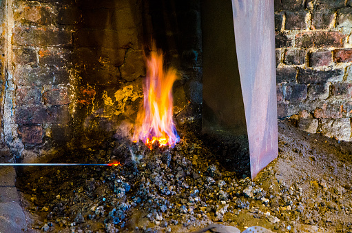 Flames coming out of firepit of smithy\nThe blacksmith is heating a metal rod