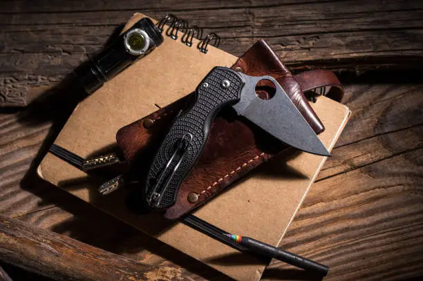 Photo of Pocket knife and leather key holder. Pencil and notebook. Black pencil and rainbow-colored lead.