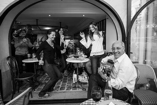 May 7, 2016 Paris, France. Café in Montmartre: Women dance and smile broadly. Small win at the cafe\n   and guitarist - live music! Maybe from Spain or Brazil - Hot Latinos!