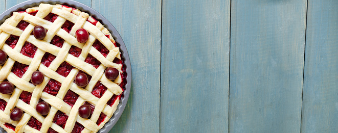 Homemade cherry pie in a round shape on a blue wooden table. The concept of traditional baking. Seasonal pie. Horizontal orientation. Top view. Copy space. Banner