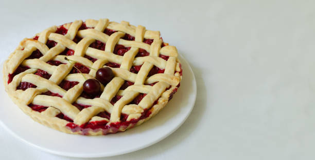 istock Homemade cherry pie on a large white plate on a white tablecloth on the table. The concept of traditional baking. Seasonal pie. Horizontal orientation. Banner. Copy space 1409552511