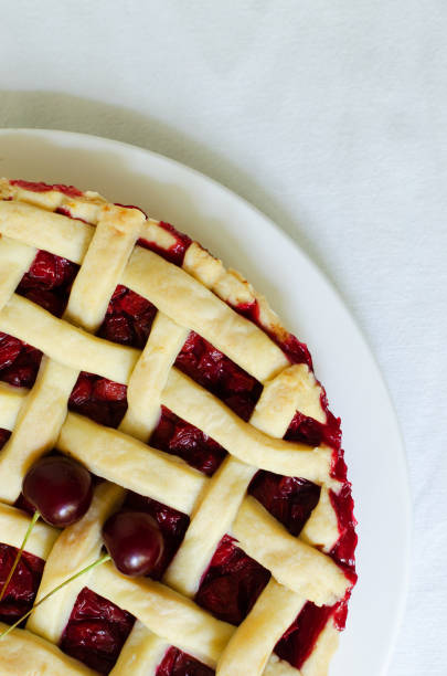 istock Homemade cherry pie on a large white plate with ribs on a white tablecloth on the table. The concept of traditional baking. Seasonal pie. Vertical orientation. Top view. 1409552512