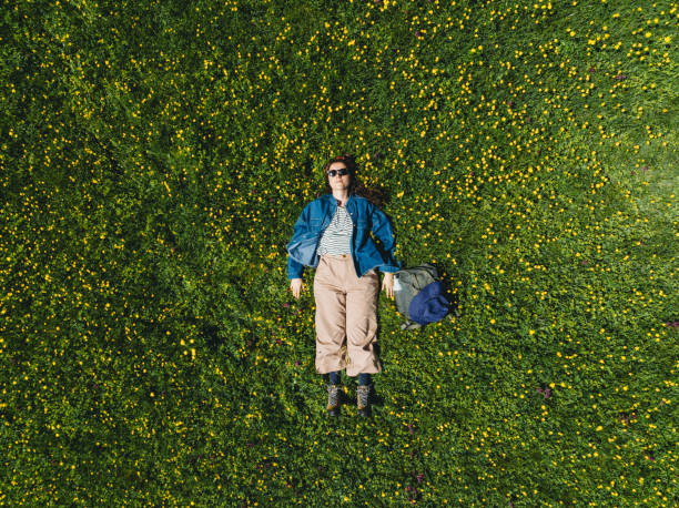 A woman is lying down on the grass surrounded by yellow flowers