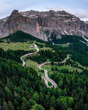 Aerial view of a winding road  with a mountain range  in the background in Val Gardena, Dolomites, Italy. S-shape road in a forest.