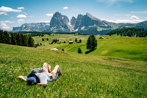 A woman is lying down on the grass in Seiser Alm, Dolomites. Alpe di Siusi with Langkofel mountain group in the background.