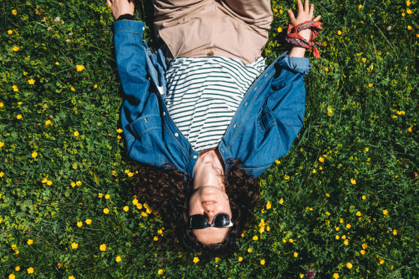 A woman is lying down on the grass surrounded by yellow flowers. Copy space.