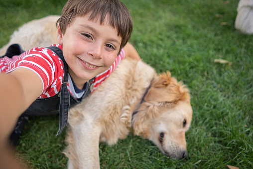 Happy little boy doing selfie with his dog on grass