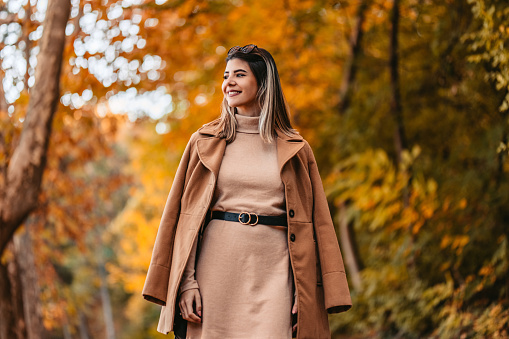 Beautiful young woman having a walk in the park during autumn.