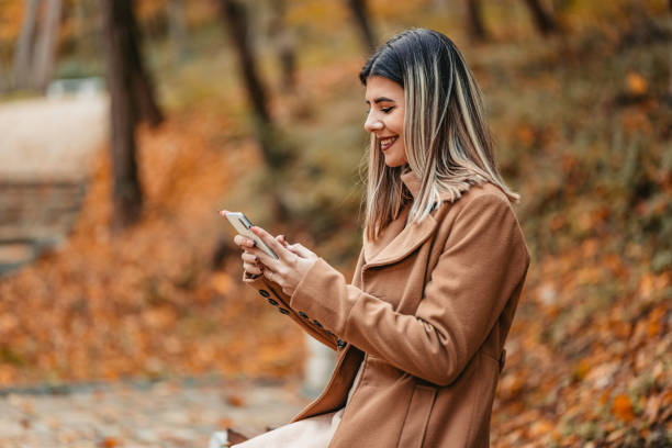 istock Young Woman Sitting In The Park And Using Phone 1409556130