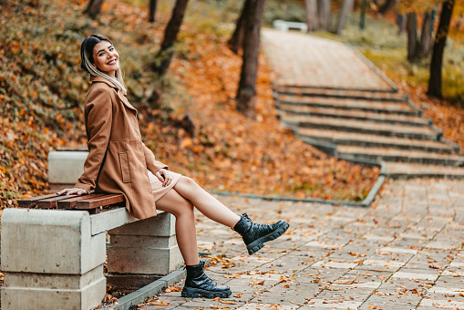 Profile of a beautiful young woman sitting on a bench in the park during autumn.