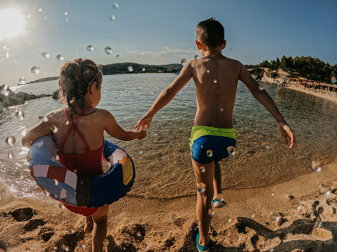 Brother with his little sister holding hands and going in the sea on summer vacation.