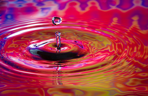 A drop of water is captured hitting a liquid abstract surface.