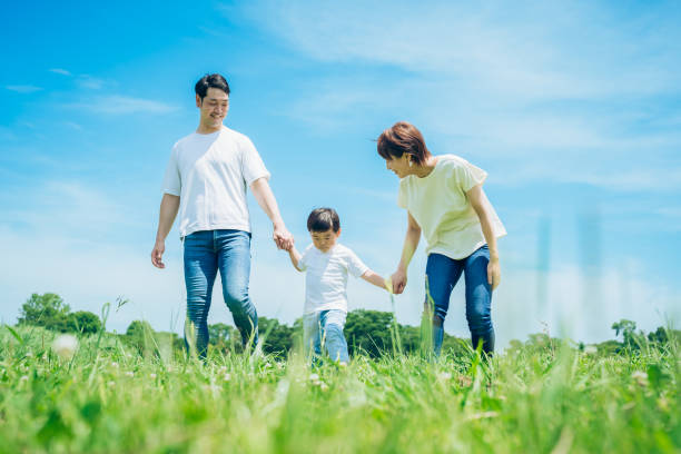 親と子が手をつないで、日当たりの良い緑地を歩く - offspring ストックフォトと画像