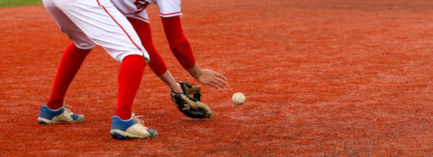 Baseball infielder fielding the ball on a red turf field A high school baseball player fielding the ball on red turf field during a game. baseball sport stock pictures, royalty-free photos & images