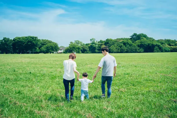 Photo of parents and their child holding hands and walking in a sunny green space