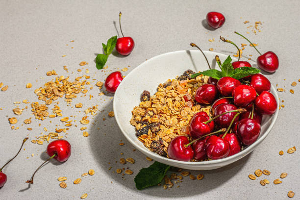 Summer breakfast concept. Healthy morning food. Ripe cherries and granola, light concrete background