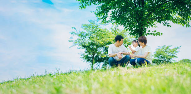 pais e seus filhos sentados em um espaço verde ensolarado - japanese ethnicity family smiling happiness - fotografias e filmes do acervo