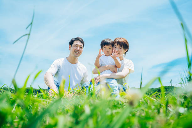 日当たりの良い緑地に座る親と子供 - three person family ストックフォトと画像