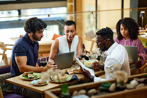 A multicultural busy businesspeople are working on a start-up project in a restaurant at the dinner table.