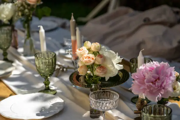 The table is set for a good party. The table is set. Empty plates and unusual glasses. Vintage tray and candleholder and vases with beautiful flowers. Close-up