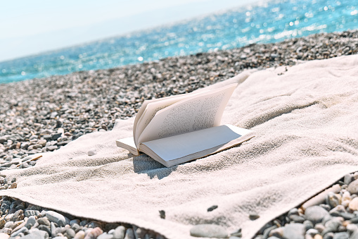 Open book on the pebble beach. Concept of reading and relaxing in summer vacation. Beach literature.