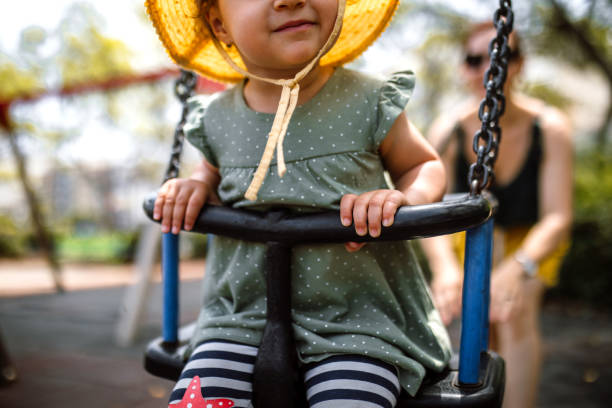 Cheerful mother pushing daughter on swing in sunny park