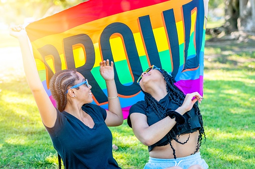 African american young lesbians holding a rainbow banner with the word Proud written on it