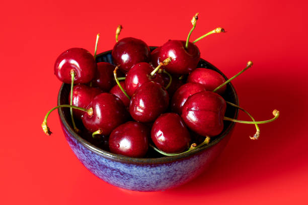 dojrzałe jagody czereśni w niebieskiej misce na czerwonym tle - drop red delicious apple apple fruit zdjęcia i obrazy z banku zdjęć