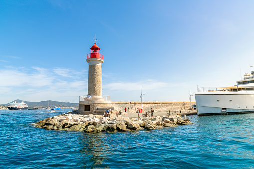 Tourists sightsee at the Phare de Saint-Tropez, the lighthouse at the edge of the harbor and Marina at Saint-Tropez on the Cote d'Azur French Riviera.