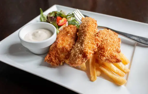 deep fried fish and chips with salad and sour sauce on white plate on table