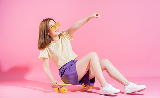 Photo of Asian teenager girl with skateboard on pink background
