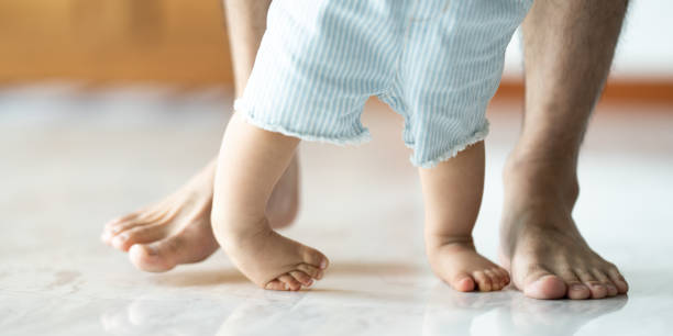 istock Baby learning to walk with father helping him learn at home by holding hand 1409596793