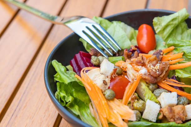 Breakfast salad with sauteed vegetables and with a fork placed on a wooden table.