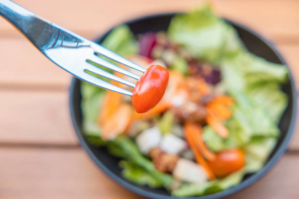 Use a fork a tomato skewer in the foreground and a salad in the background. Breakfast salad with sauteed vegetables on a wooden table.