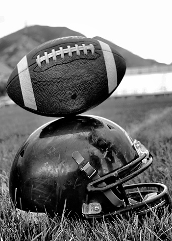 Monochromatic football balancing on helmet on football field, conceptual image.