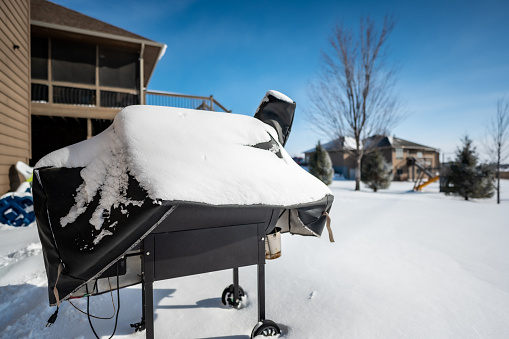 Snow covered BBQ smoker grill in the backyard with winter background