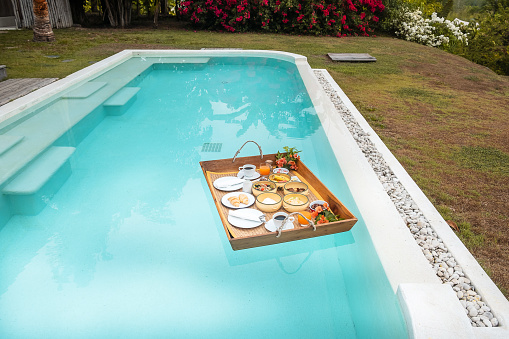 Floating Breakfast tray in swimming pool at luxury hotel or tropical resort villa, fruits, croissant, coffee, and orange juice. Exotic summer, relaxation, tropical travel and vacation concept