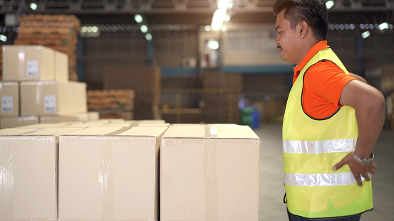 Asian man worker in a warehouse have an accident while carrying a heavy cardboard boxes with careless, male worker have a critical accident and injured at his back.