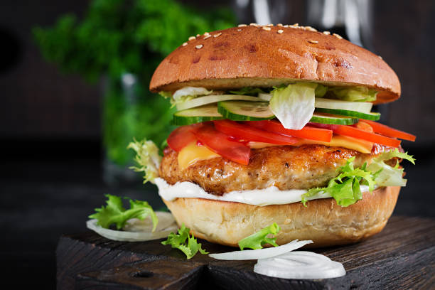 istock Hamburger with chicken burger meat, cheese, tomato, cucumber and lettuce on wooden background. Tasty burger. Close up 1409620607