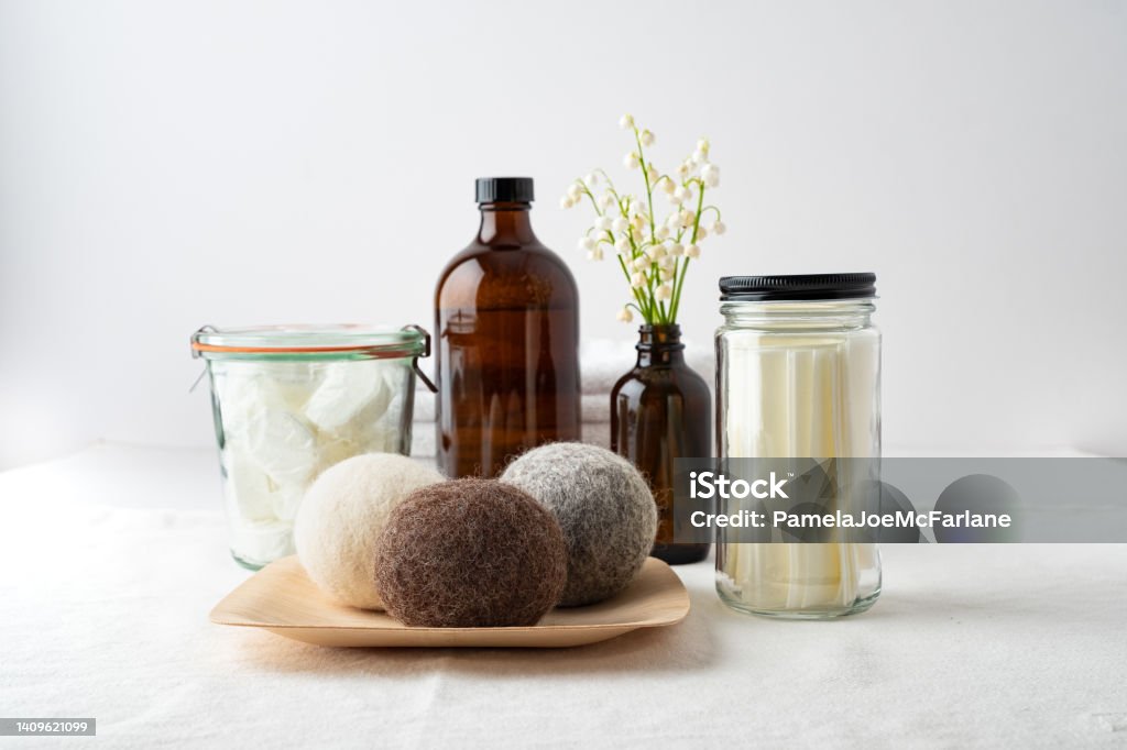 Zero Waste Laundry Tablets, Soap, Sheets and Dryer Balls Eco-friendly laundry products: dishwasher tablets in dissolvable wrappers stored in mason jar, liquid laundry soap in refillable bottle, laundry soap sheets in re-useable jar, wool dryer balls on bamboo plate, flower arrangement in re-useable bottle. Laundry Stock Photo