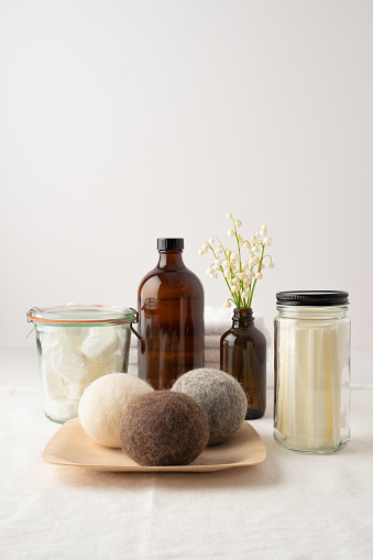 Eco-friendly laundry products: dishwasher tablets in dissolvable wrappers stored in mason jar, liquid laundry soap in refillable bottle, laundry soap sheets in re-useable jar, wool dryer balls on bamboo plate, flower arrangement in re-useable bottle.