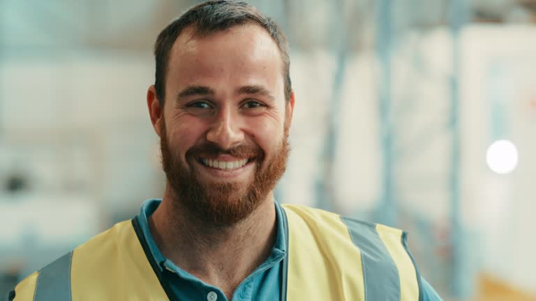 Portrait of happy male engineers face in a production warehouse. Smiling professional male heavy industry engineer wearing a safety helmet standing smiling and looking confident in a workshop factory