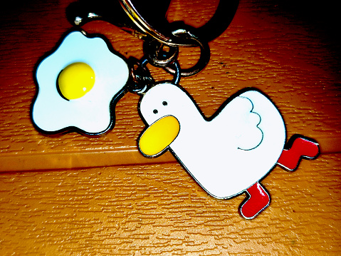 Close up photo of a key ring with a duck's  and egg icons. Object using a brown wooden table background