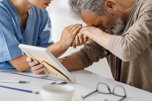 Female home caregiver consoling depressed senior man.