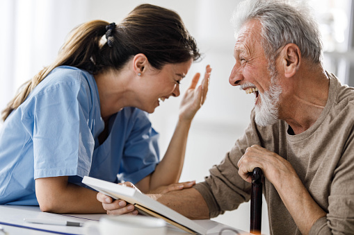 Cheerful female nurse and senior man having fun while talking about something funny in retirement home.