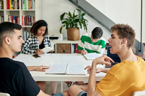 Deaf friends doing homework together Focus on foreground teenage boys in casual clothing sitting at dining table and communicating about their assignment. Part of lifestyle series depicting deaf family and friends. deaf stock pictures, royalty-free photos & images