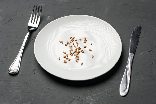 Concept of a global food crisis caused by hunger due to lack of grain. Plate with small amount of grain on plate on black background Concept of a global food crisis caused by hunger due to lack of grain. Plate with small amount of grain on plate on black background, close up reducing the appetite stock pictures, royalty-free photos & images