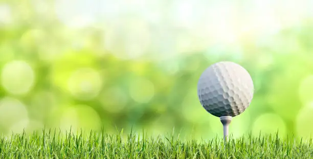 Golf ball on tee with grass and green blurred background